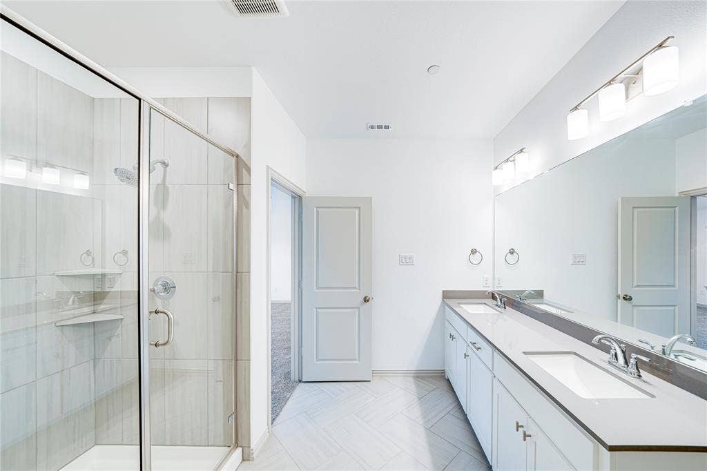 8888 Samara Street, Frisco, TX 75035 Glass-enclosed shower with tiled walls and built-in shelving, dual vanity with undermount sinks and extensive countertop space, full-width mirror, and tiled flooring