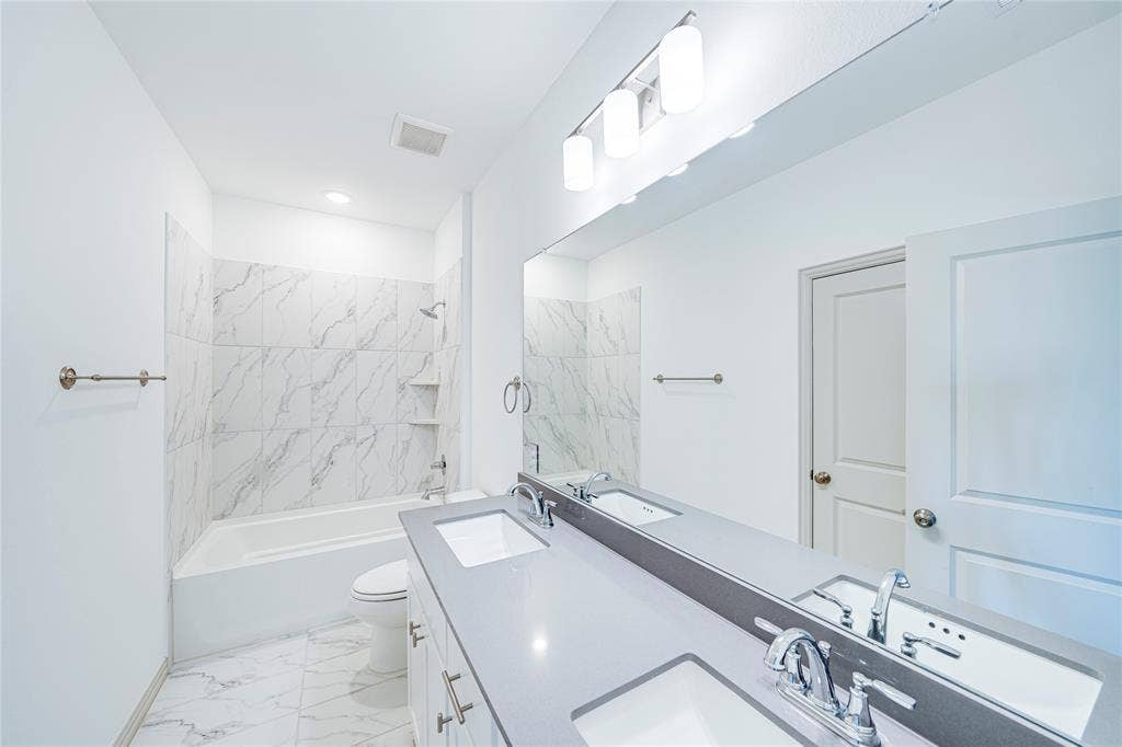 8888 Samara Street, Frisco, TX 75035 Dual vanity with undermount sinks and chrome fixtures, large wall-mounted mirror, three-light vanity bar, integrated tub/shower with tiled surround, and white floor tiling