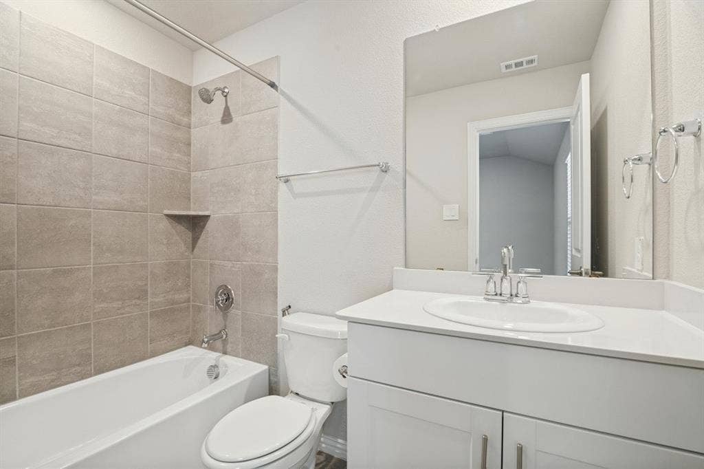 753 Poppy Lane, Lavon, TX 75166 Bathroom featuring a white vanity with a composite countertop and integrated sink, a large wall-mounted mirror, and a tub-shower combination with floor-to-ceiling textured tile surrounds