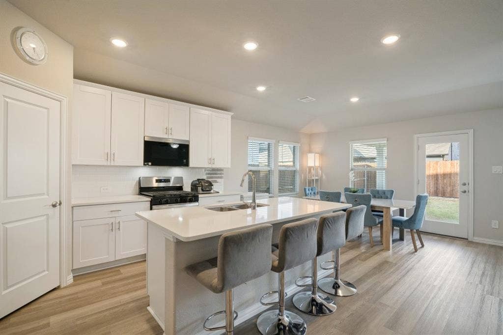 753 Poppy Lane, Lavon, TX 75166 Kitchen featuring white cabinetry, an expansive central island with a solid-surface countertop, integrated undermount sink, recessed lighting, and wood-finish flooring
