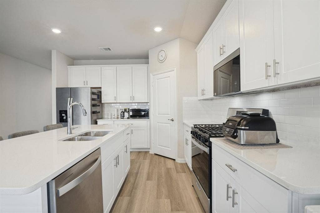 753 Poppy Lane, Lavon, TX 75166 Kitchen featuring white shaker-style cabinetry, solid-surface countertops, subway tile backsplash, stainless steel appliances, and wood-finish flooring