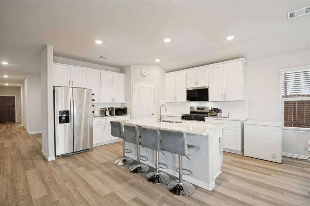 753 Poppy Lane, Lavon, TX 75166 Kitchen featuring white cabinetry, center island with stone-finish countertop and integrated sink, stainless steel refrigerator, and wood-finish flooring