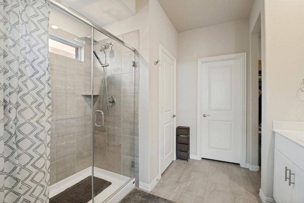 753 Poppy Lane, Lavon, TX 75166 Walk-in shower with floor-to-ceiling tile surround, glass enclosure, and rainfall showerhead, complemented by wood-finish flooring and white vanity cabinetry with metallic pulls