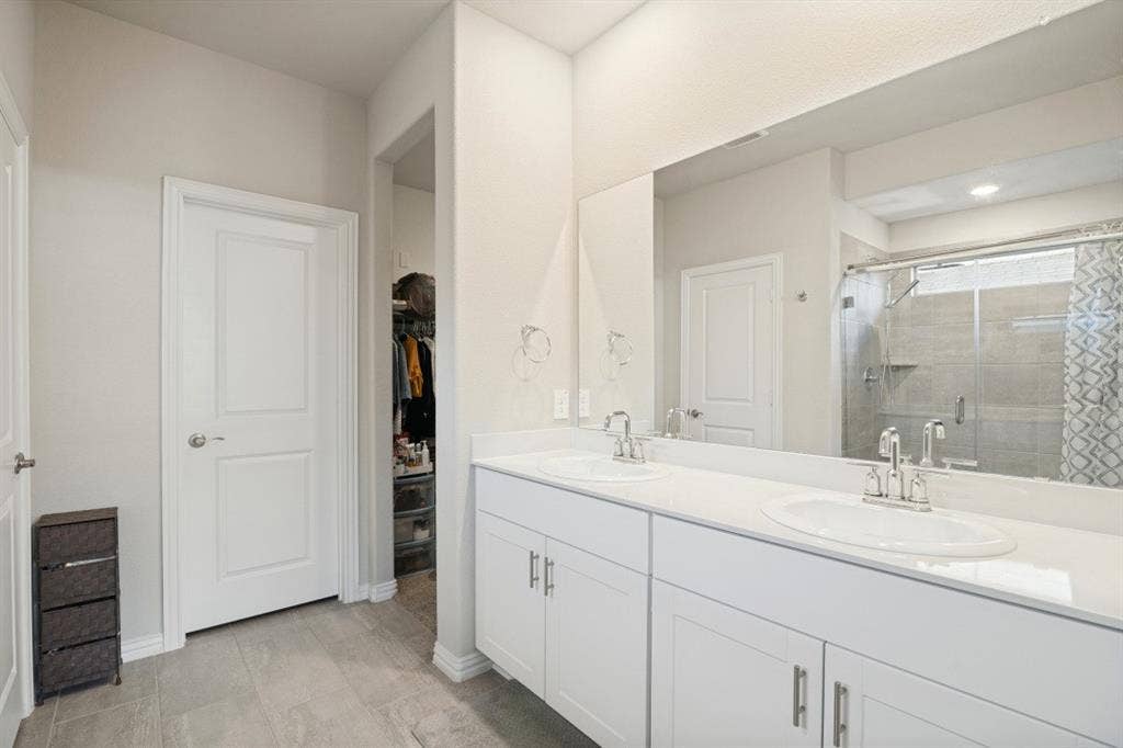 753 Poppy Lane, Lavon, TX 75166 Dual vanity with white cabinetry, rectangular solid-surface countertop, integrated sinks, full-width mirror, and tiled shower surround with glass enclosure