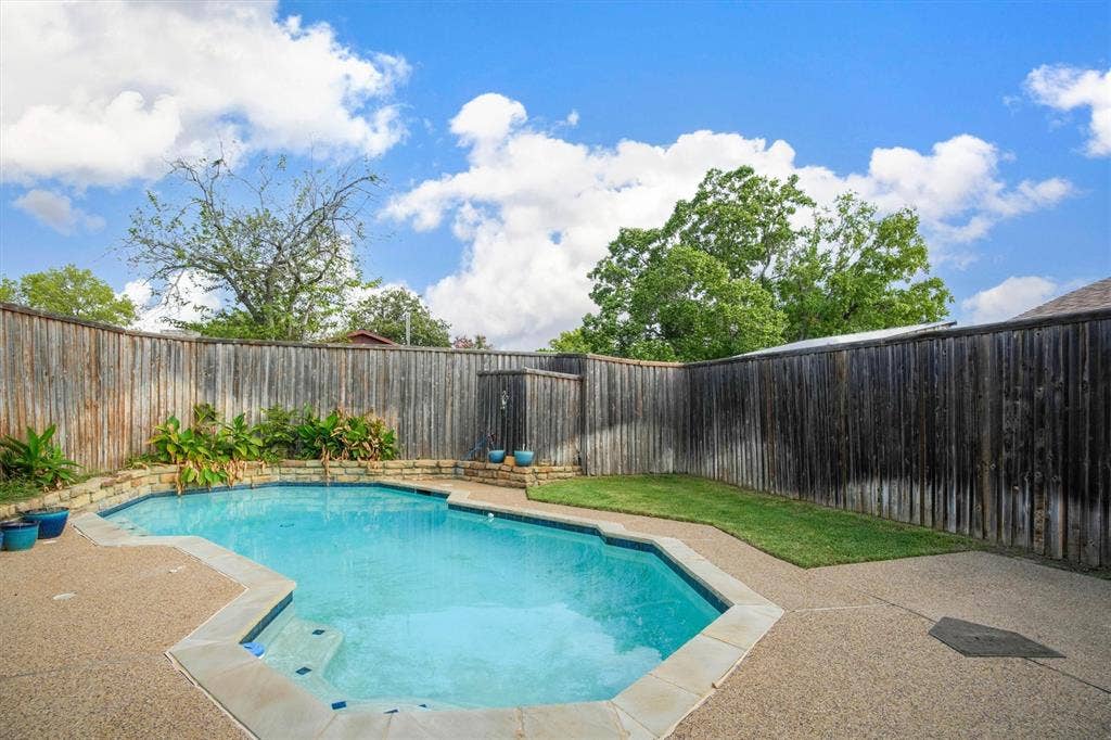 In-ground swimming pool with stone coping, textured concrete pool deck, retaining wall with integrated plantings, and perimeter wood fencing