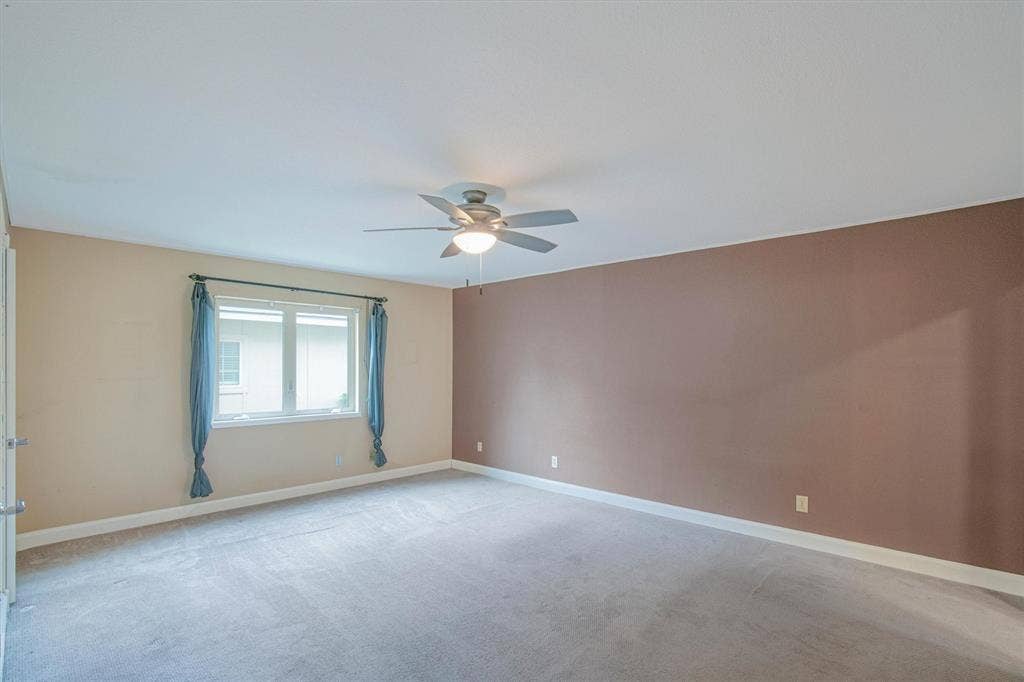 Interior space featuring neutral wall tones, a large window, wall-to-wall carpeting, and a ceiling-mounted light fixture with fan blades