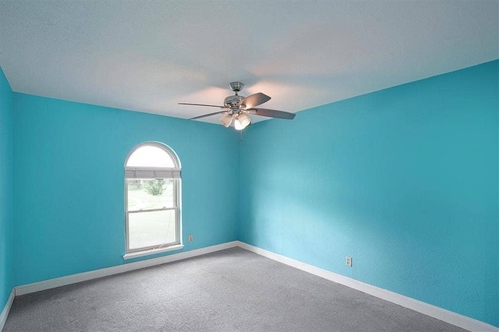 Room featuring an arched window, carpeted flooring, and a ceiling-mounted light fixture with a fan