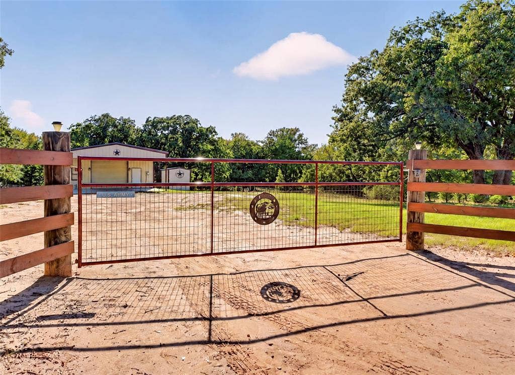 Front gate entry with wood posts and metal fencing, featuring a metal building with an attached shed