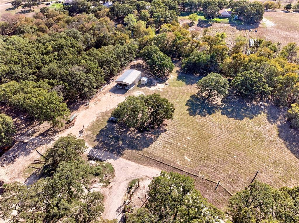 Expansive natural landscape featuring a metal-roofed structure, mature trees, and a dirt pathway