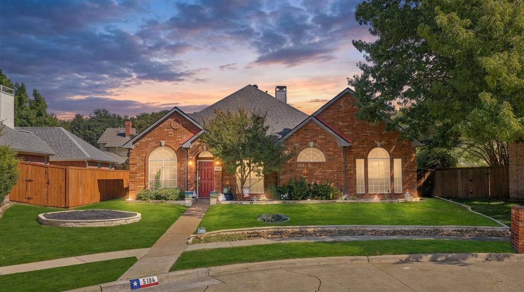 5104 Teddington Park Drive, Plano, TX 75023 Brick exterior with arched windows, a red entry door, a gabled roof, and a stone-edged lawn