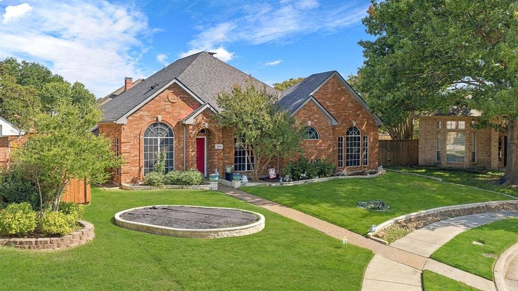 5104 Teddington Park Drive, Plano, TX 75023 Brick exterior with arched windows, dark roofing, and a manicured lawn featuring a circular ground-level element