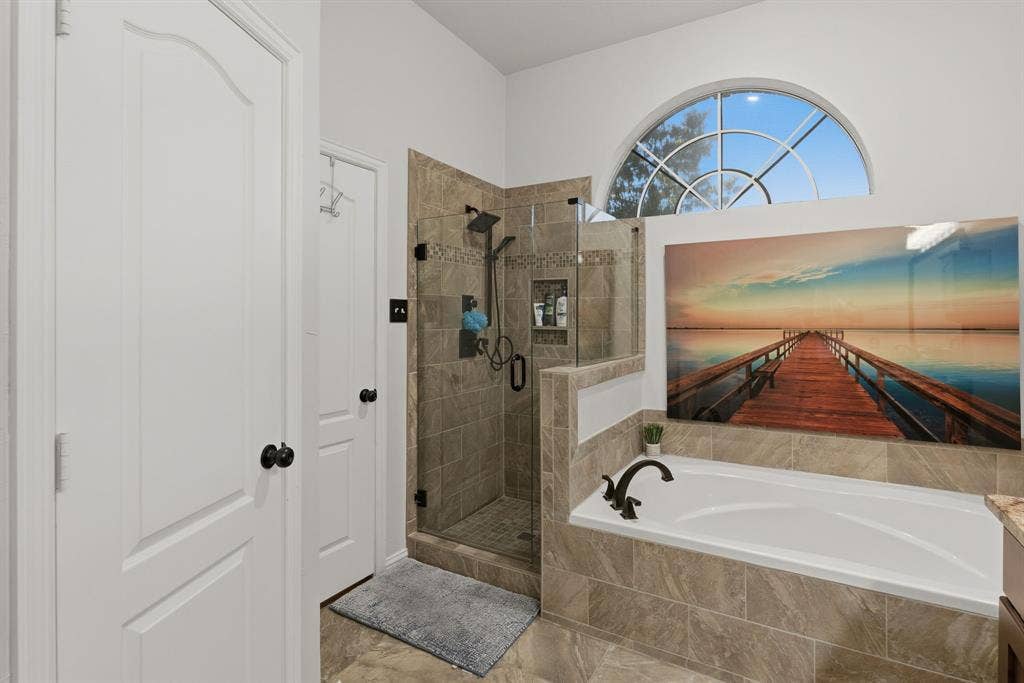 5104 Teddington Park Drive, Plano, TX 75023 Tile-surround soaking tub with bronze-finish fixtures, a tiled shower enclosure with a glass door, and a decorative arched window