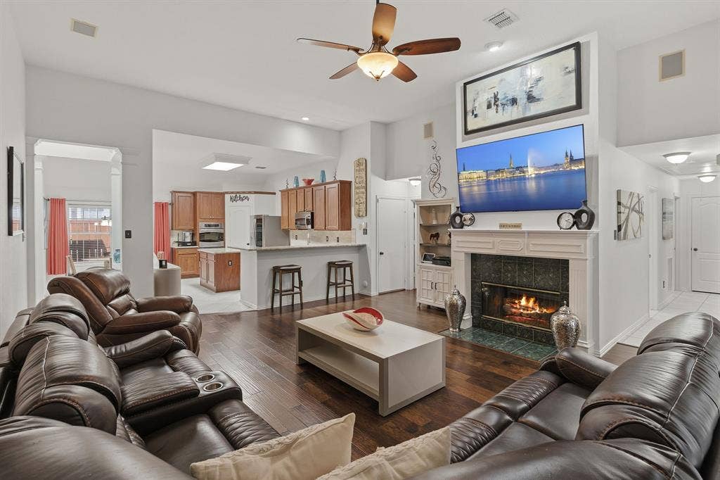 5104 Teddington Park Drive, Plano, TX 75023 Vaulted ceiling with a ceiling fan, fireplace with a decorative mantel and tile surround, wood-finish flooring, recessed lighting, and a kitchen with wood cabinetry and a breakfast bar