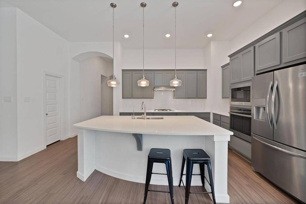 1553 Wyler Drive, Forney, TX 75126 Kitchen featuring an expansive island with a white countertop, gray cabinetry, stainless steel appliances, and wood-finish flooring