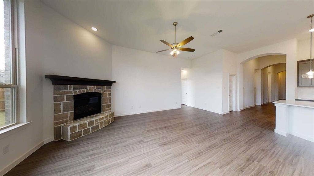 1553 Wyler Drive, Forney, TX 75126 Stone-clad fireplace with dark wood mantel, wood-finish flooring, recessed lighting, ceiling fan, and arched entryway