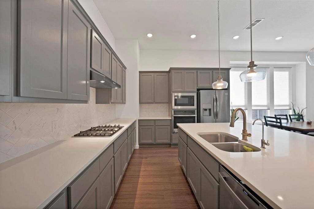 1553 Wyler Drive, Forney, TX 75126 Contemporary kitchen featuring gray shaker cabinetry, stainless steel appliances, a gas cooktop, and a spacious island with a double basin sink