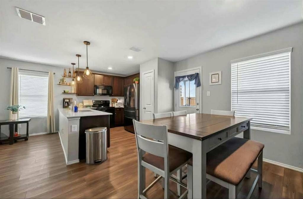 554 Deerfern Drive, Princeton, TX 75407 Open-concept kitchen and dining area featuring wood-finish flooring, dark wood cabinetry, a center island with pendant lighting, and black appliances