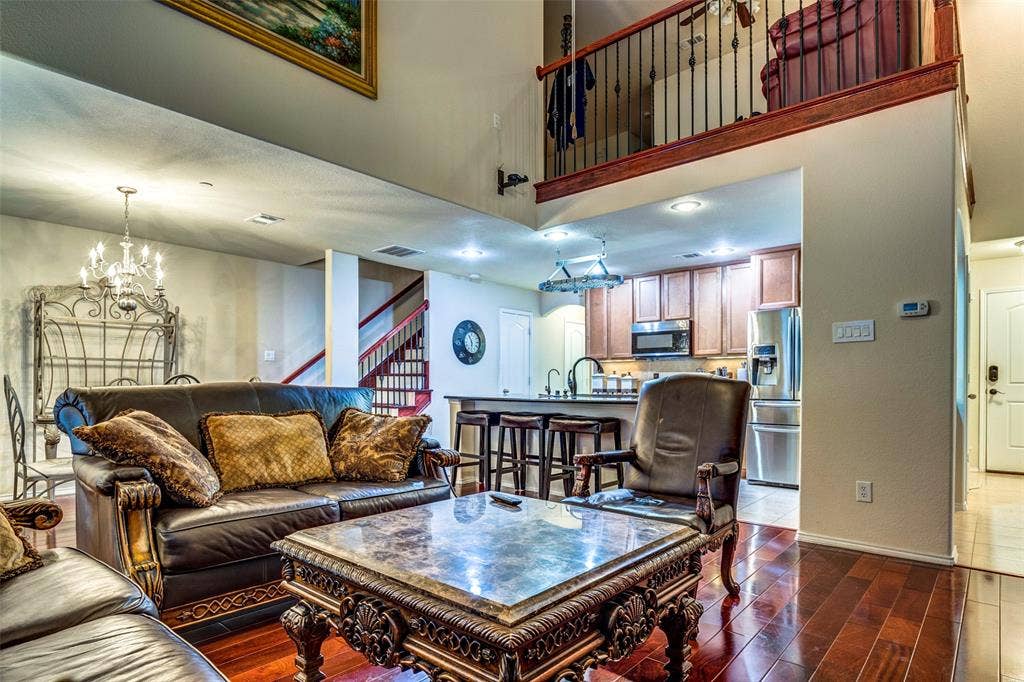 1040 Lucy Lane, Allen, TX 75013 Two-story living area with wood-finish flooring, an upper-level balcony, and a visible kitchen featuring stainless steel appliances and wood cabinetry