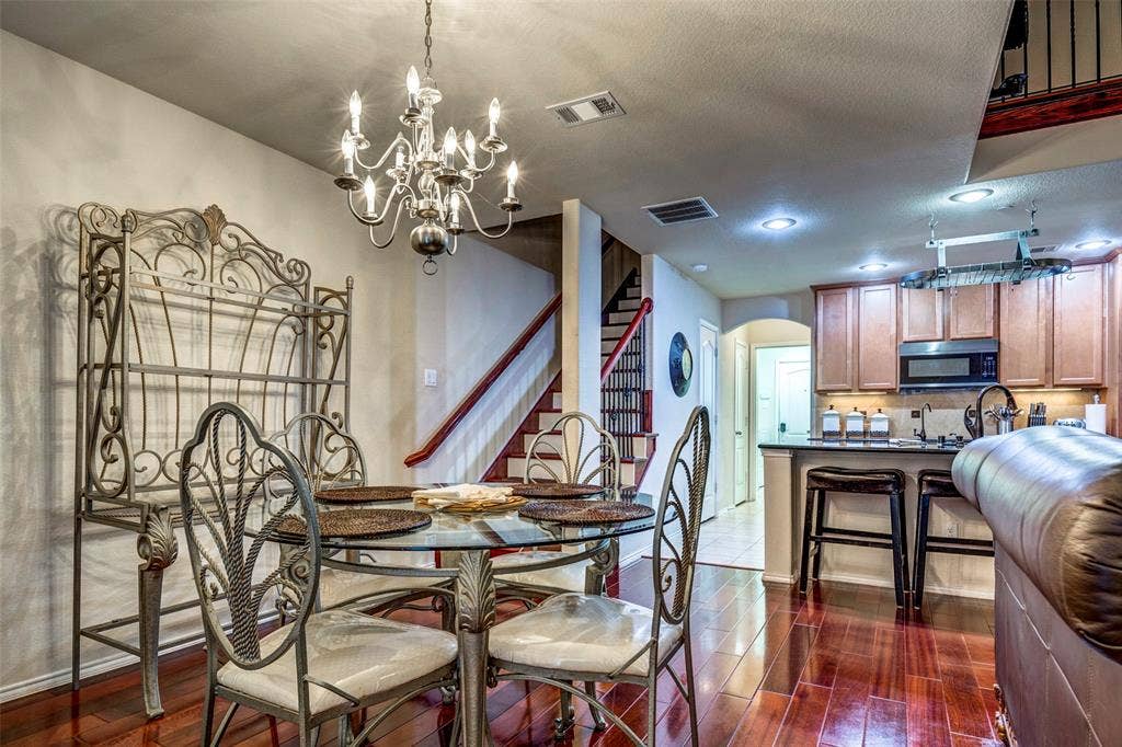 1040 Lucy Lane, Allen, TX 75013 Open-concept dining and kitchen area featuring a round glass-top table with ornamental metal base and chairs, wood-finish flooring, pendant lighting, stainless steel appliances, wood cabinetry, and a curved archway entry