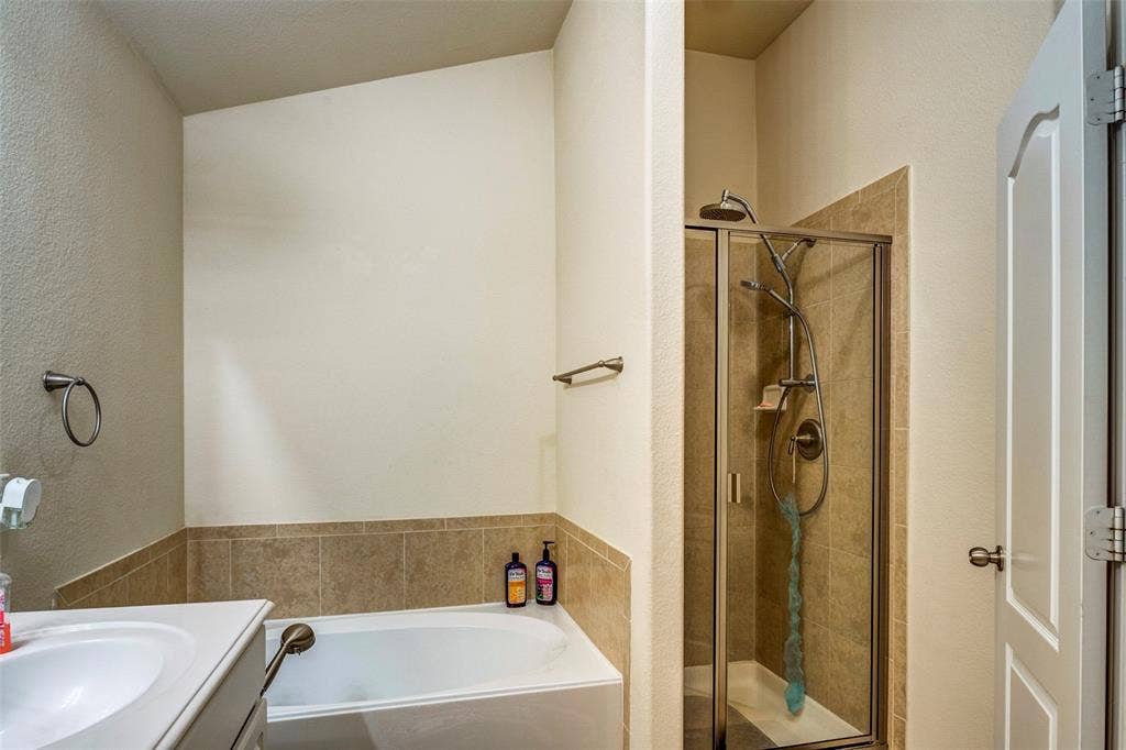 1040 Lucy Lane, Allen, TX 75013 Master bathroom featuring dual vanity with white ceramic sink, tile-accented wall surround, soaking tub, and separate walk-in shower with glass enclosure and bronze fixtures