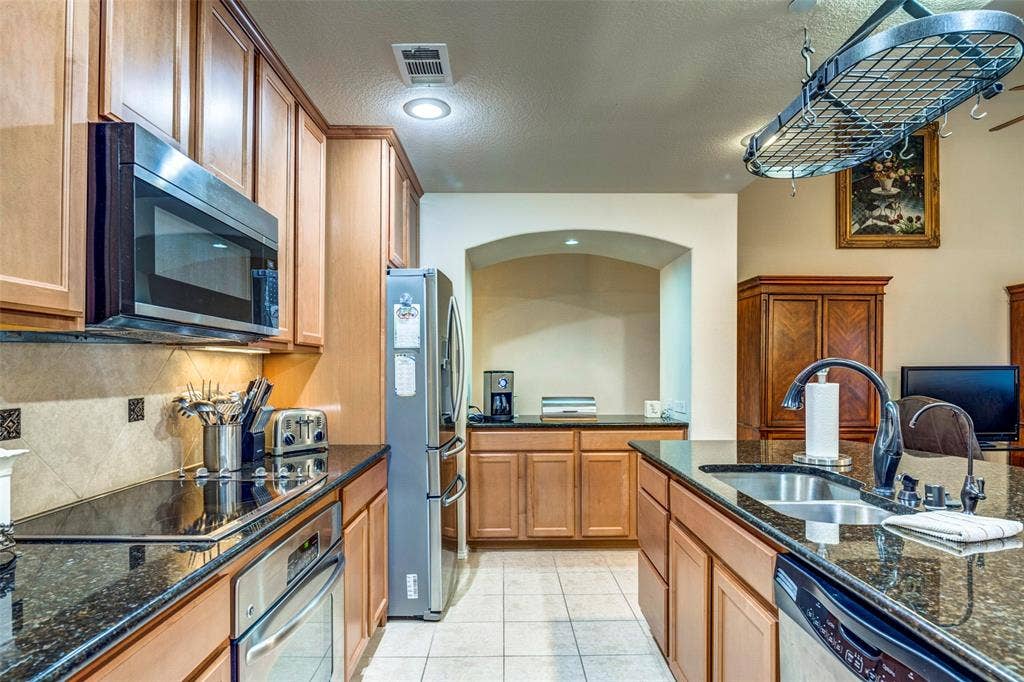 1040 Lucy Lane, Allen, TX 75013 Kitchen featuring wood cabinetry, dark countertops, tile flooring, and stainless steel appliances