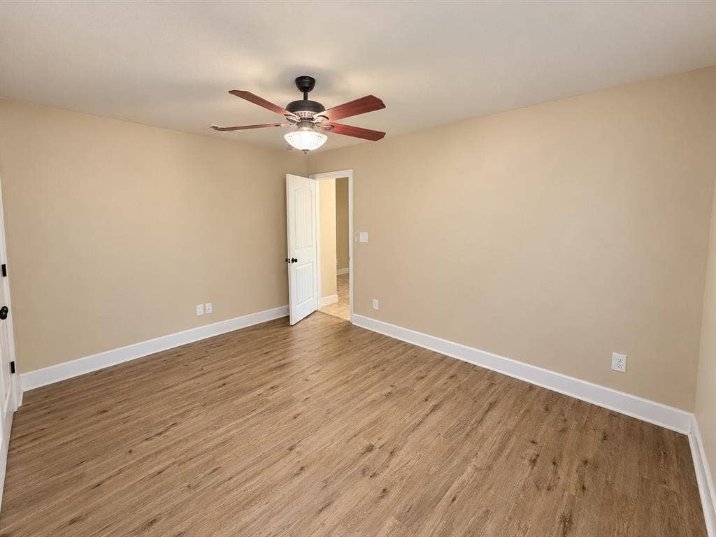 Wood-finish flooring, neutral wall paint, ceiling fan with integrated lighting, and white trim