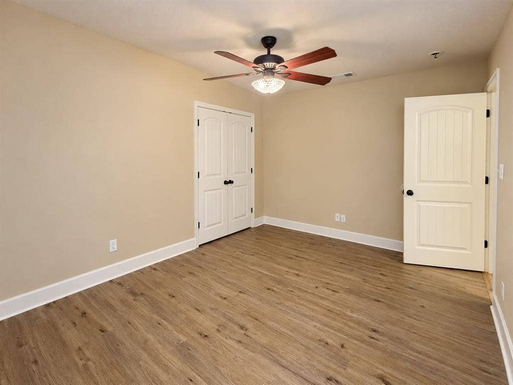 Wood-finish flooring, neutral wall tones, white trim, ceiling fan with integrated lighting, and white paneled doors with dark hardware