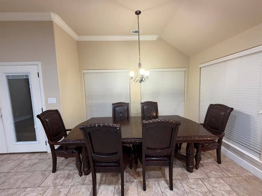 Vaulted ceiling with crown molding, durable tile flooring, and multiple windows