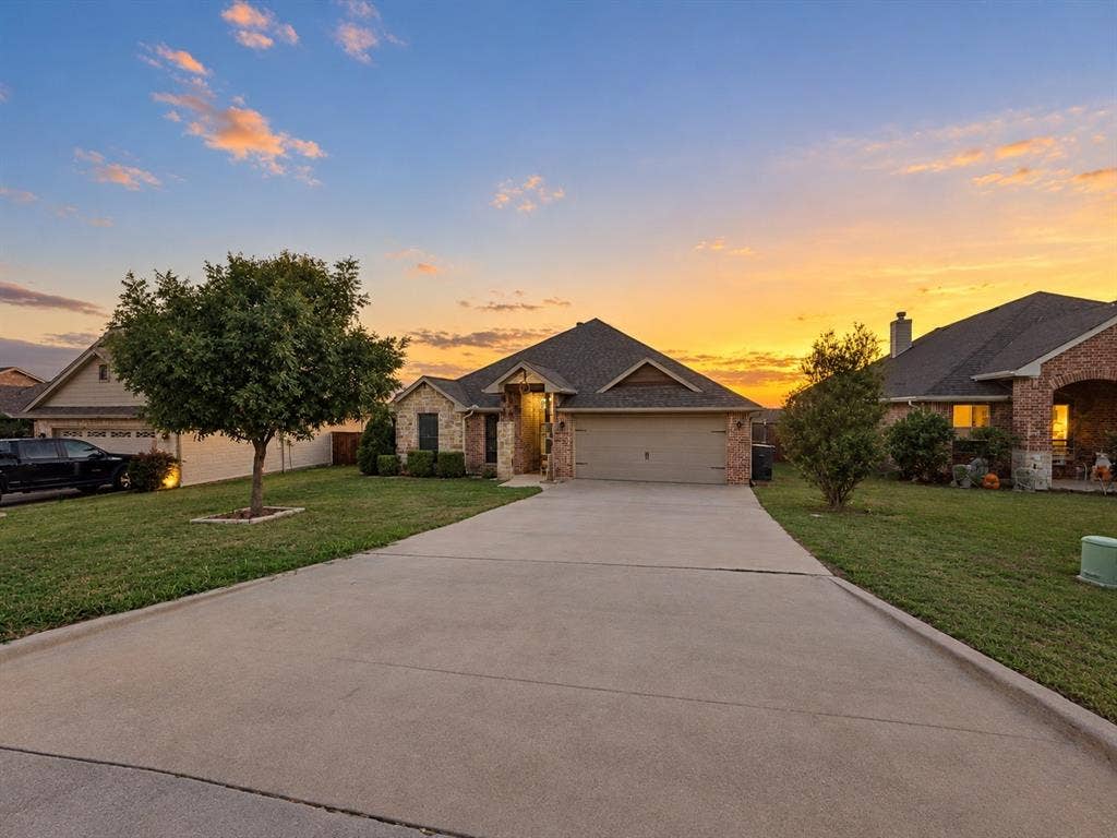 Brick and stone exterior with an attached garage, pitched shingle roof, and a concrete driveway