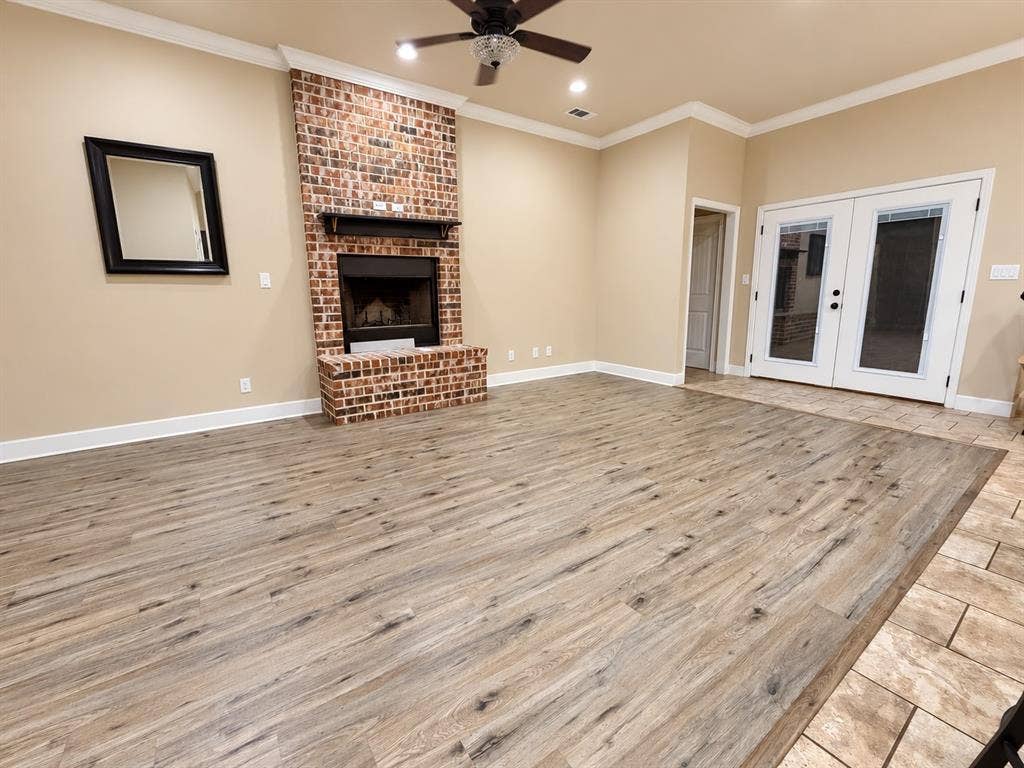 Brick fireplace with a wooden mantel, wood-finish flooring, recessed lighting, ceiling fan, and French doors with integrated blinds