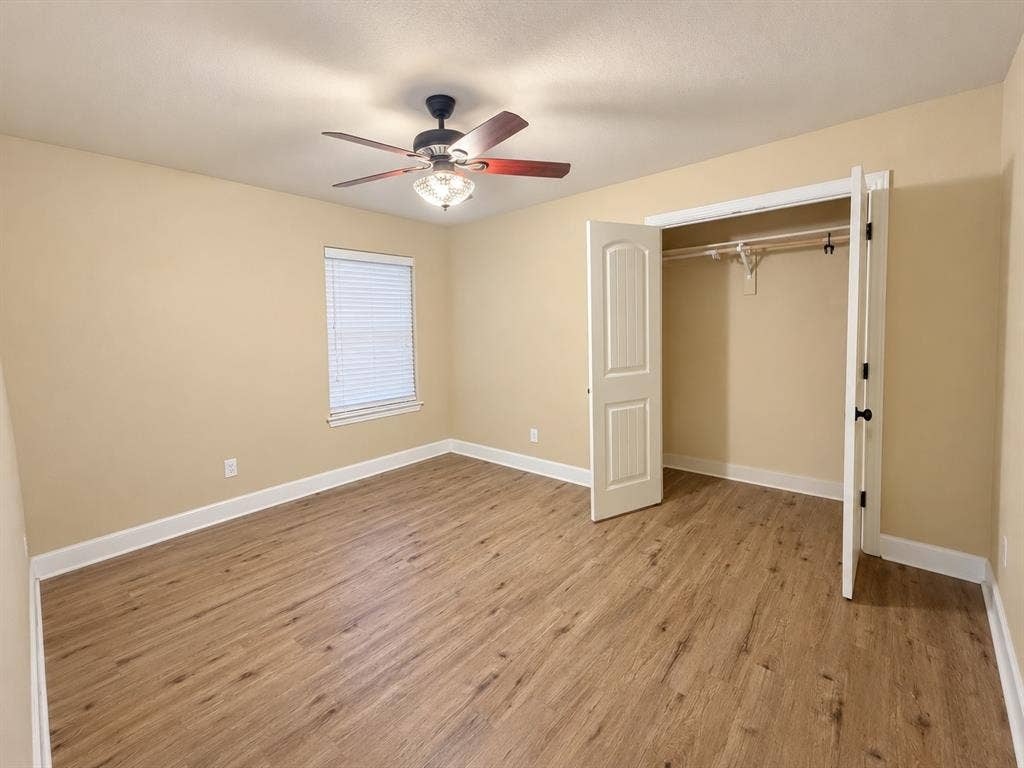 Wood-finish flooring, ceiling fan, window with blinds, and a closet with bifold doors