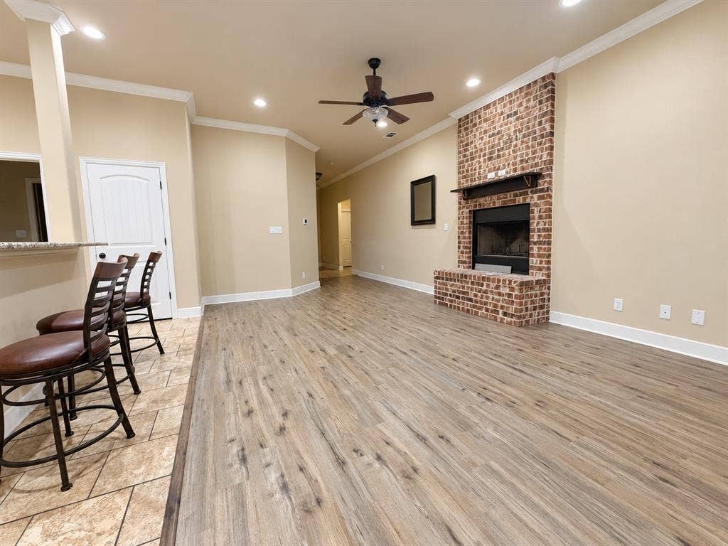 Open-concept living space featuring wood-finish flooring, a brick-surround fireplace with a mantel, and recessed lighting