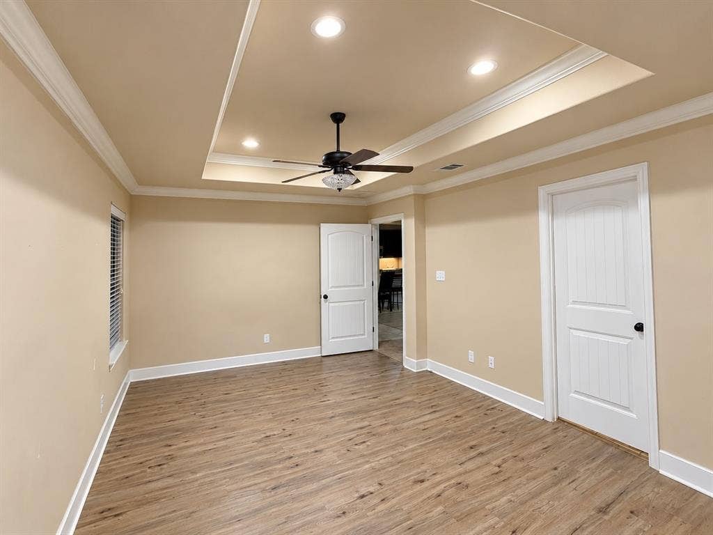 Tray ceiling with recessed lighting, crown molding, wood-finish flooring, ceiling fan, and white paneled doors