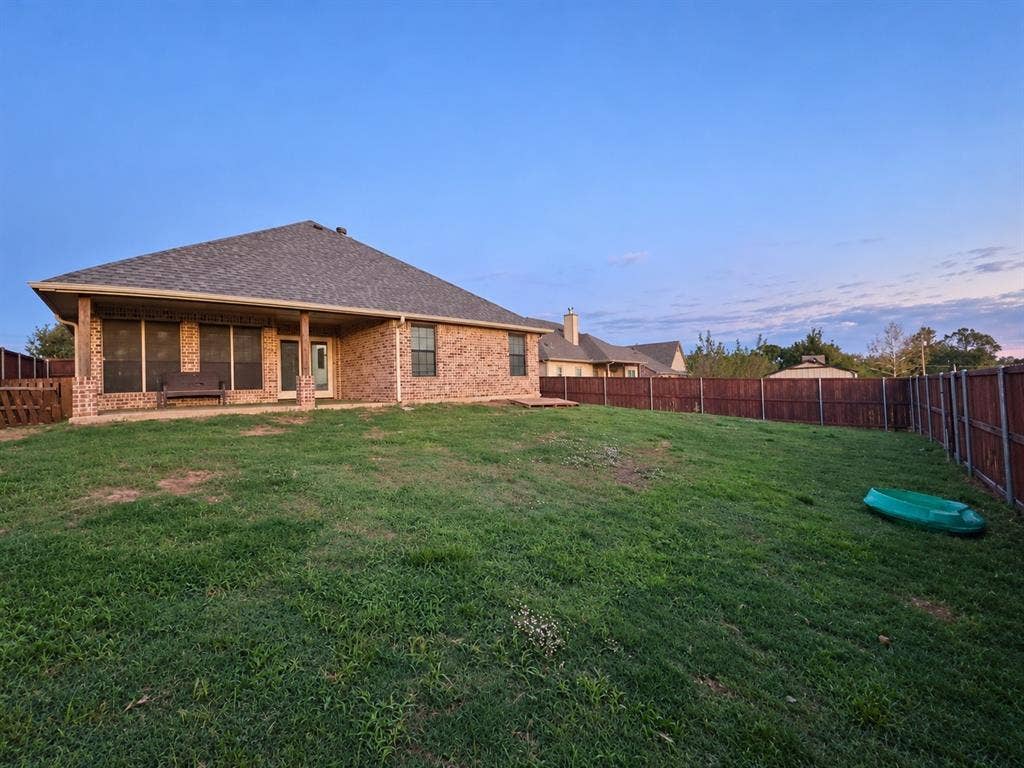 Brick exterior with a covered patio, fenced backyard, and a shingled roof
