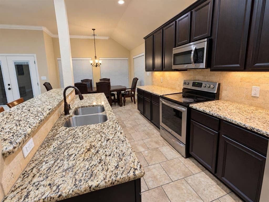 Kitchen featuring dark wood-finish cabinetry, light-toned granite countertops, and stainless steel appliances