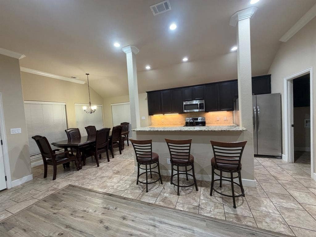 Vaulted ceiling featuring a chandelier, tile flooring, wood-finish flooring, and a kitchen pass-through with built-in cabinetry and stainless steel appliances