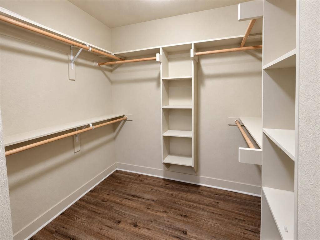 Walk-in closet featuring wood-finish flooring, built-in shelving, and multiple hanging rods