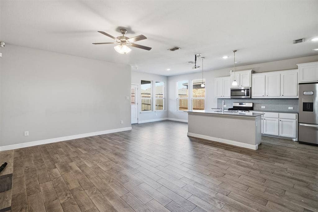 2513 Foules Drive, Glenn Heights, TX 75154 Open-concept living area featuring wood-finish flooring, a contemporary kitchen island, white cabinetry, stainless steel appliances, and a ceiling fan