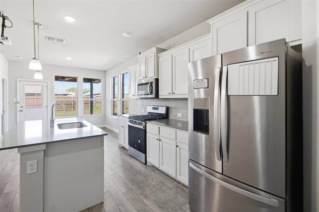 2513 Foules Drive, Glenn Heights, TX 75154 Kitchen featuring white cabinetry, stainless steel appliances, a center island with sink, grey countertops, and wood-finish flooring