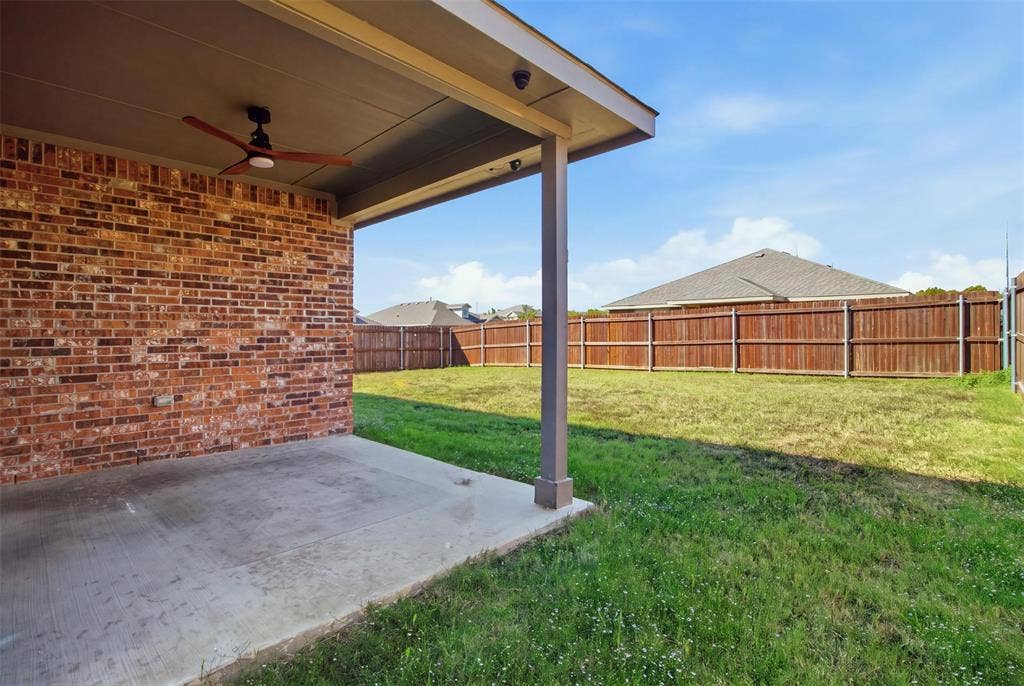 2513 Foules Drive, Glenn Heights, TX 75154 Covered patio with a ceiling fan, brick exterior, concrete flooring, and an expansive grassy yard with a wood privacy fence