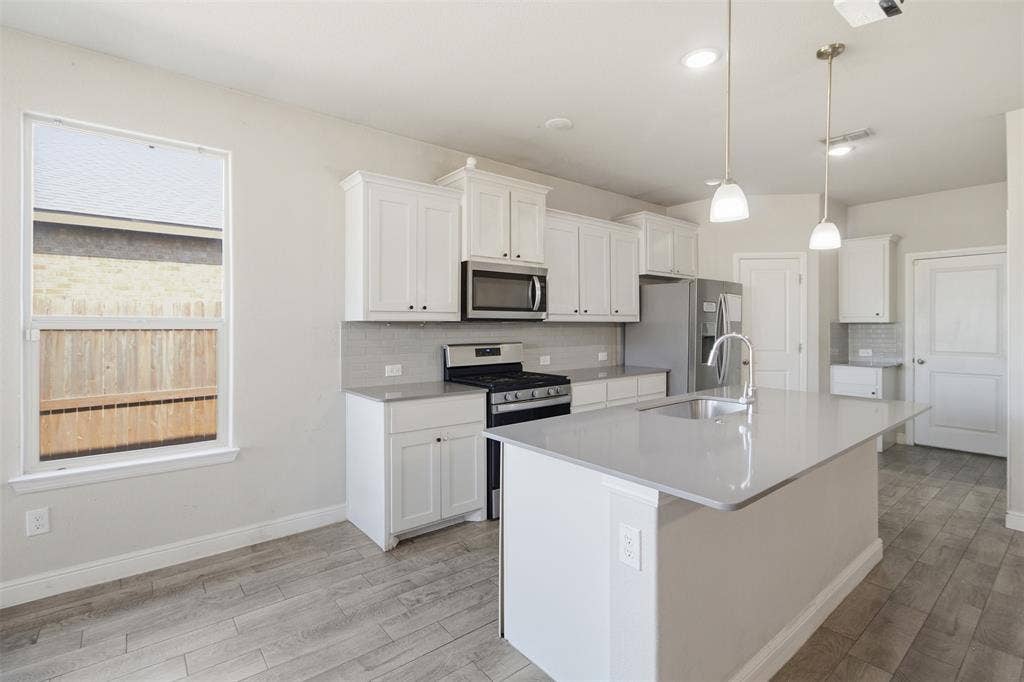 2513 Foules Drive, Glenn Heights, TX 75154 Kitchen featuring white cabinetry, stainless steel appliances, a center island with sink, pendant lighting, and wood-finish flooring