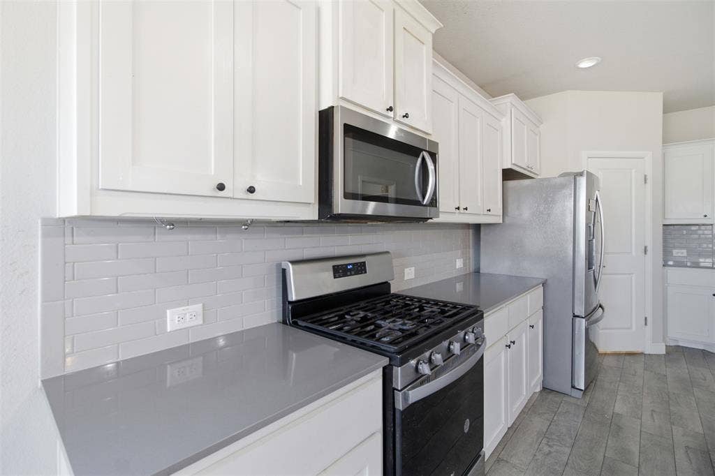 2513 Foules Drive, Glenn Heights, TX 75154 White shaker cabinetry, grey subway tile backsplash, stainless steel appliances, grey countertops, and wood-finish flooring