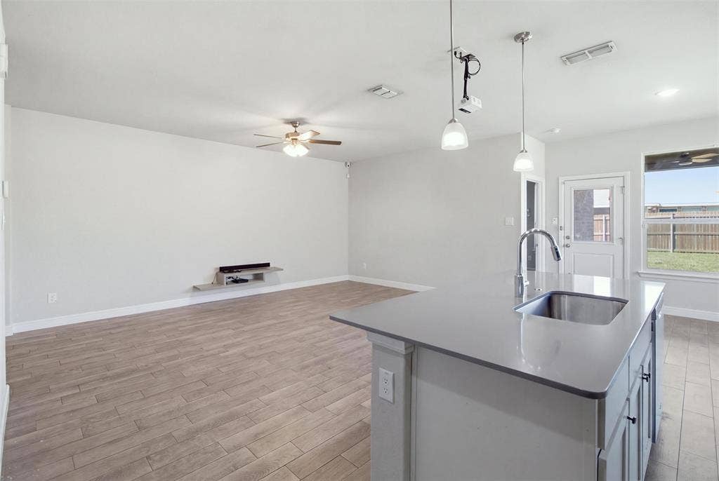 2513 Foules Drive, Glenn Heights, TX 75154 Open-concept living space featuring wood-finish flooring, a ceiling fan, and an island with an undermount sink, gooseneck faucet, and pendant lighting
