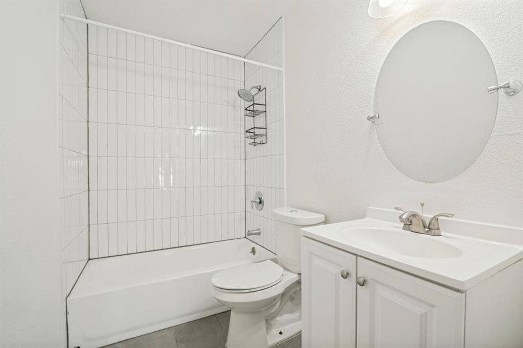 4420 Cochise Drive, Balch Springs, TX 75180 Bathroom featuring a white vanity with integrated sink, brushed nickel faucet, oval mirror, and a white bathtub with subway tile surround
