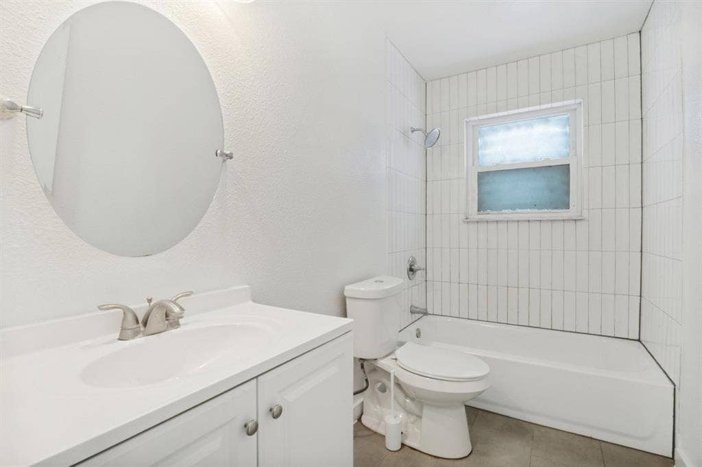 4420 Cochise Drive, Balch Springs, TX 75180 Vanity with integrated sink and brushed nickel faucet, wall-mounted oval mirror, tiled tub-shower combination, and window with privacy glass