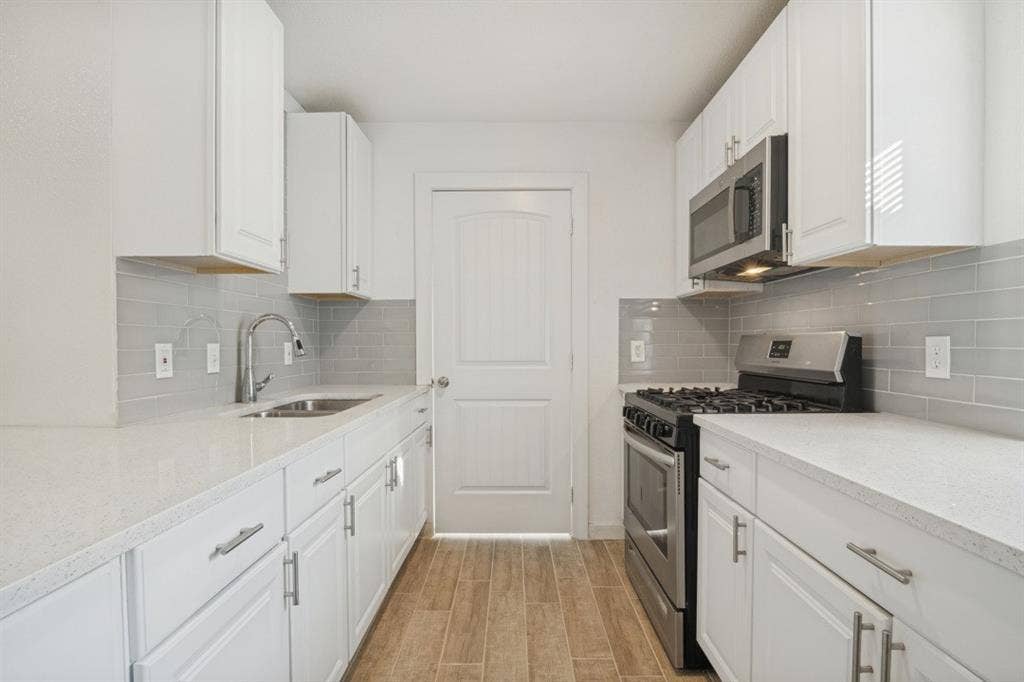 4420 Cochise Drive, Balch Springs, TX 75180 White cabinetry with brushed nickel hardware, stainless steel appliances, stone countertops, gray subway tile backsplash, and wood-finish flooring