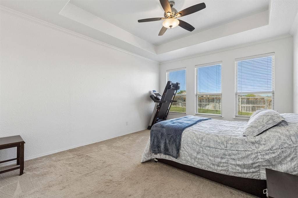 1501 Coyote Ridge Road, Wylie, TX 75098 Tray ceiling with a ceiling fan, three windows, and neutral carpeting