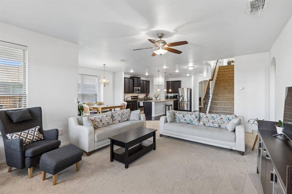 1501 Coyote Ridge Road, Wylie, TX 75098 Open-concept living area with carpet flooring and a ceiling fan, featuring a dining area with a chandelier, and a kitchen with dark cabinetry, stainless steel appliances, and a central island with pendant lighting