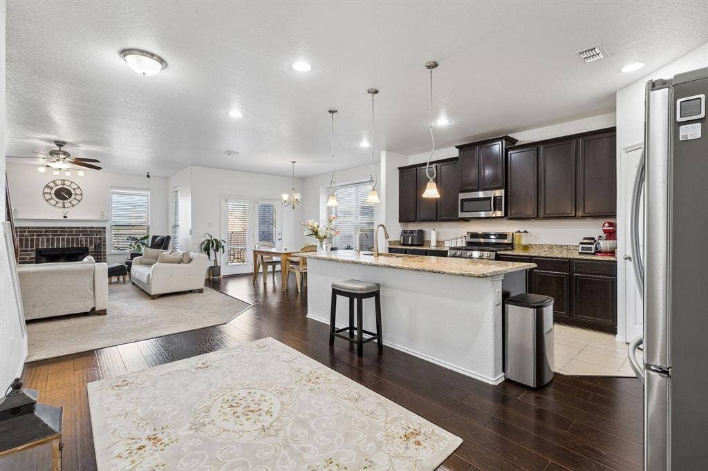 1501 Coyote Ridge Road, Wylie, TX 75098 Open-concept design featuring wood-finish flooring, a kitchen island with seating, dark wood cabinetry, and stainless steel appliances