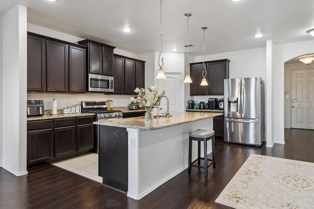 1501 Coyote Ridge Road, Wylie, TX 75098 Kitchen featuring dark wood-finish cabinetry, stainless steel appliances, a center island with granite countertop, and wood-finish flooring